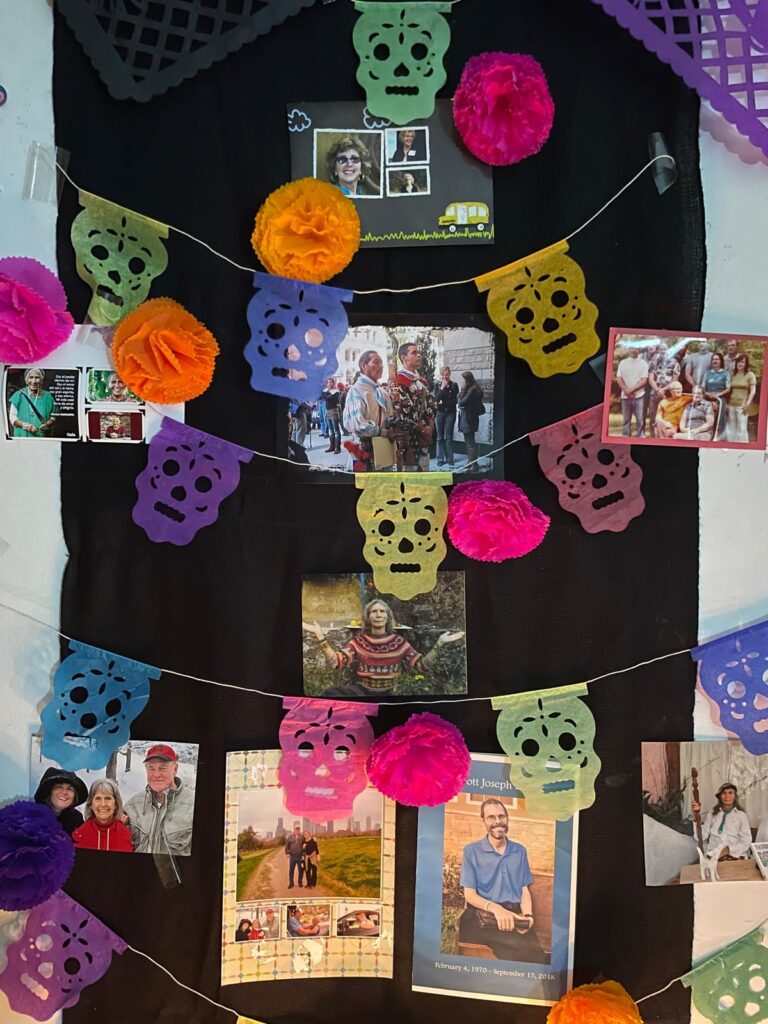 Primer plano de un altar del Día de Muertos con coloridas guirnaldas de calaveras de papel y retratos de familiares y amigos fallecidos expuestos sobre un fondo negro, simbolizando el recuerdo y la conexión.