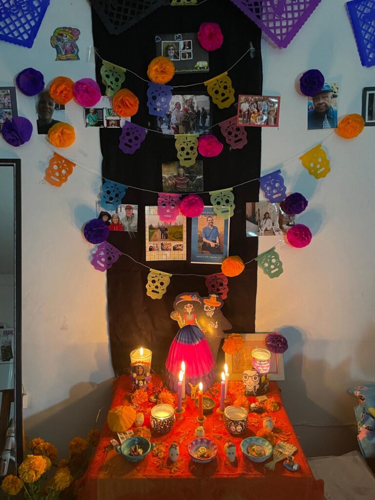 Altar del Día de Muertos decorado con cempasúchiles, velas, coloridas calaveras de papel y fotografías de seres queridos fallecidos, dispuestos sobre un mantel naranja en una casa de Guadalajara.